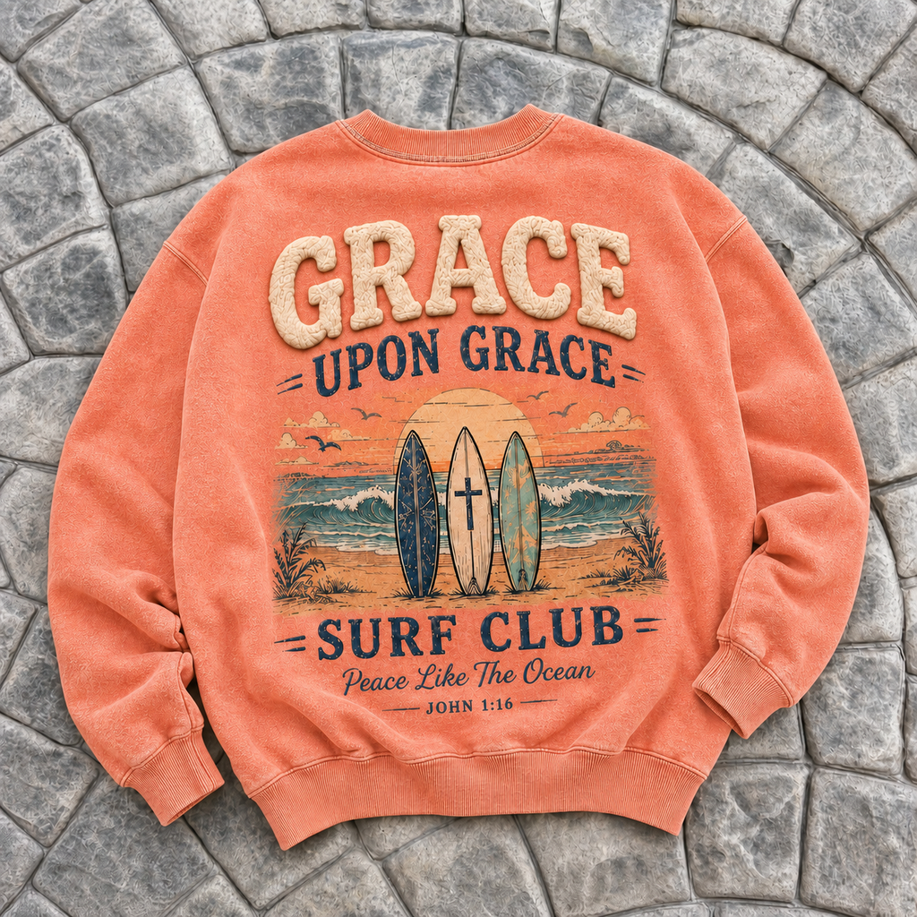 Coral-colored crewneck with 'Grace Upon Grace Surf Club' design on a stone surface