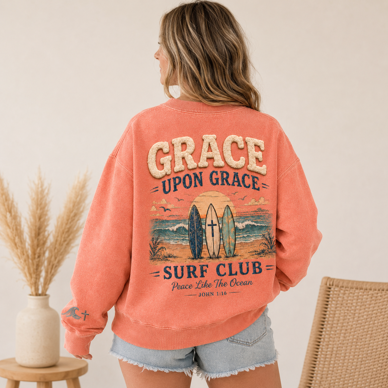 woman wearing a coral 'Grace Upon Grace Surf Club' crewneck with a beach graphic.