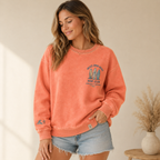 Woman wearing a coral crewneck with a graphic design, standing indoors.