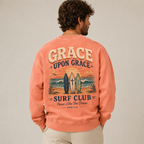 Man wearing a coral crewneck with 'Grace Upon Grace Surf Club' design on the back.