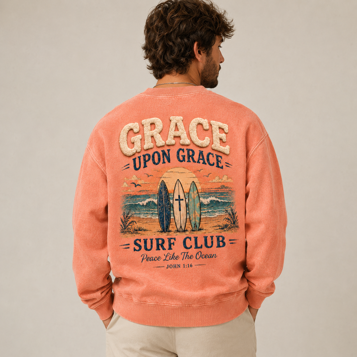 Man wearing a coral crewneck with 'Grace Upon Grace Surf Club' design on the back.