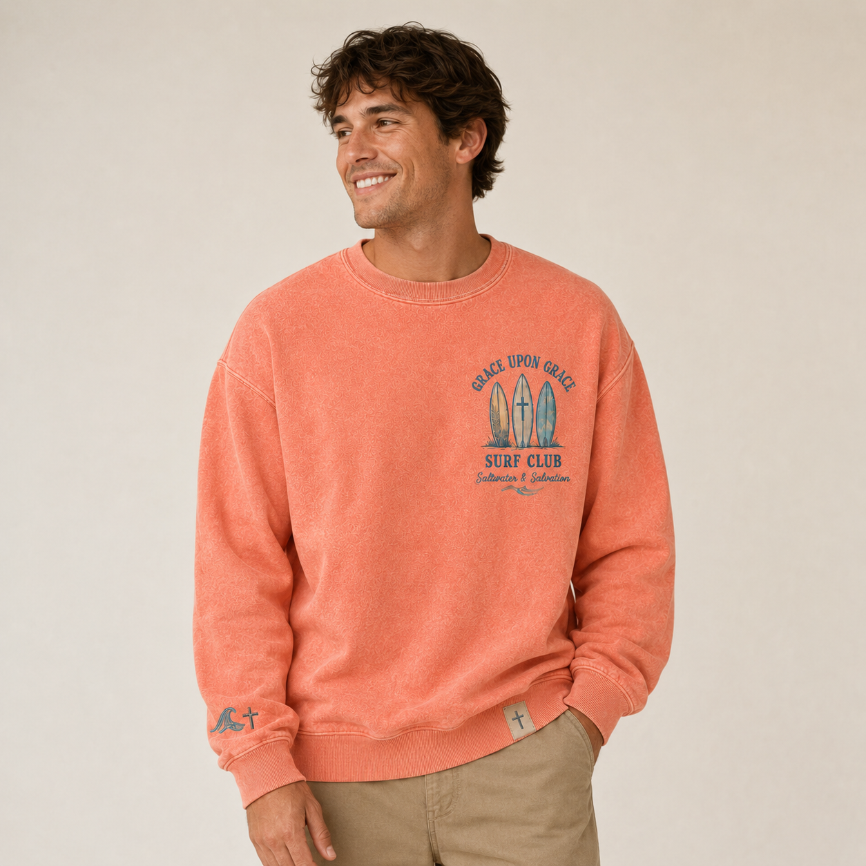 Man wearing a coral crewneck with a graphic design on a beige background