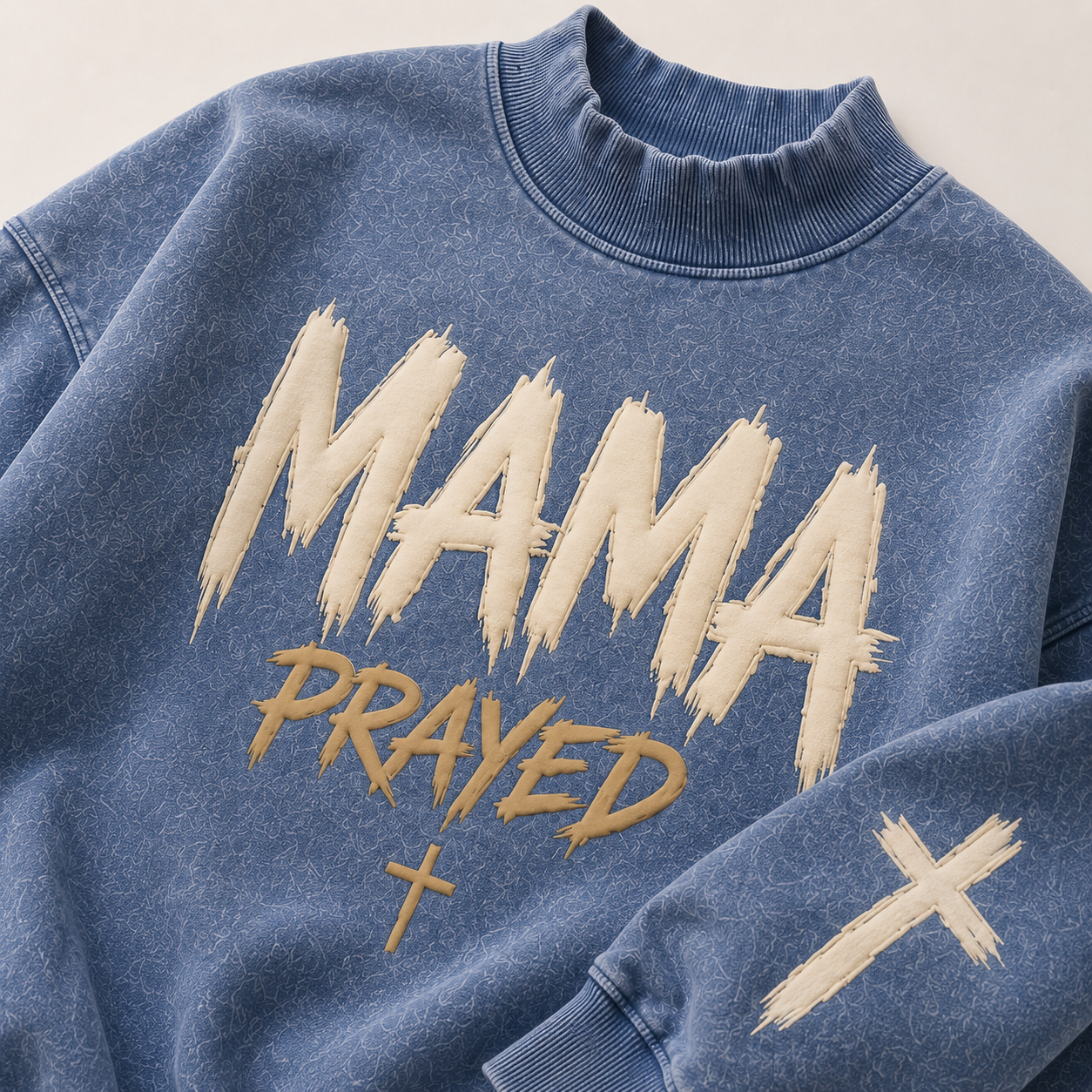 Blue sweatshirt with 'MAMA PRAYED' text in beige on a light background