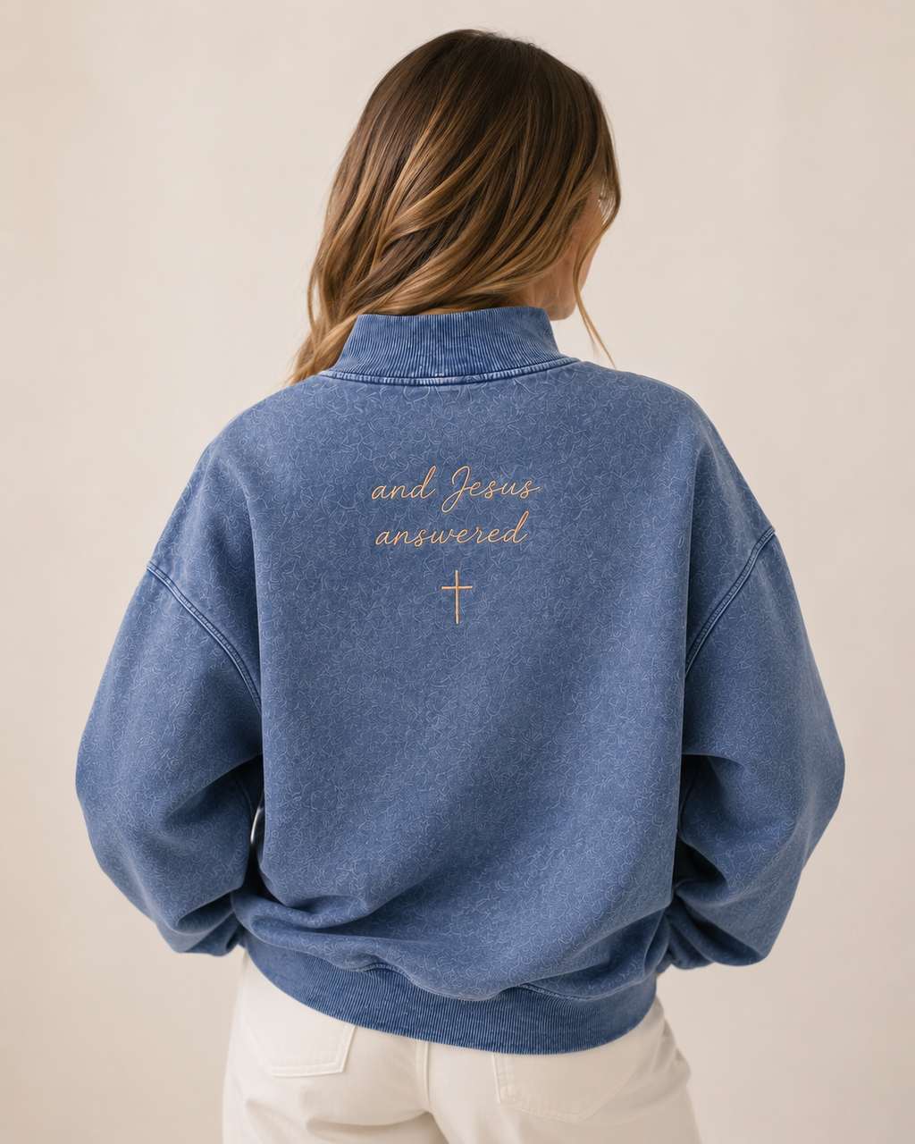 Person wearing a blue denim jacket with text and a cross on the back against a beige background