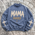 Blue sweatshirt with 'MAMA PRAYED' text and cross symbols on a stone surface