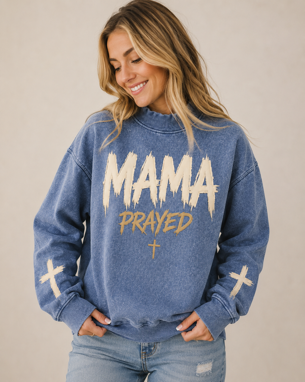 Woman wearing a blue sweatshirt with 'MAMA PRAYED' text and crosses on a beige background